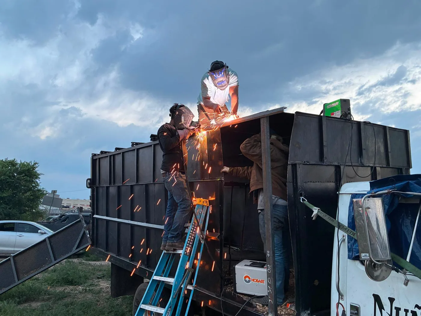Team welding structural repairs on a dump trailer at dusk