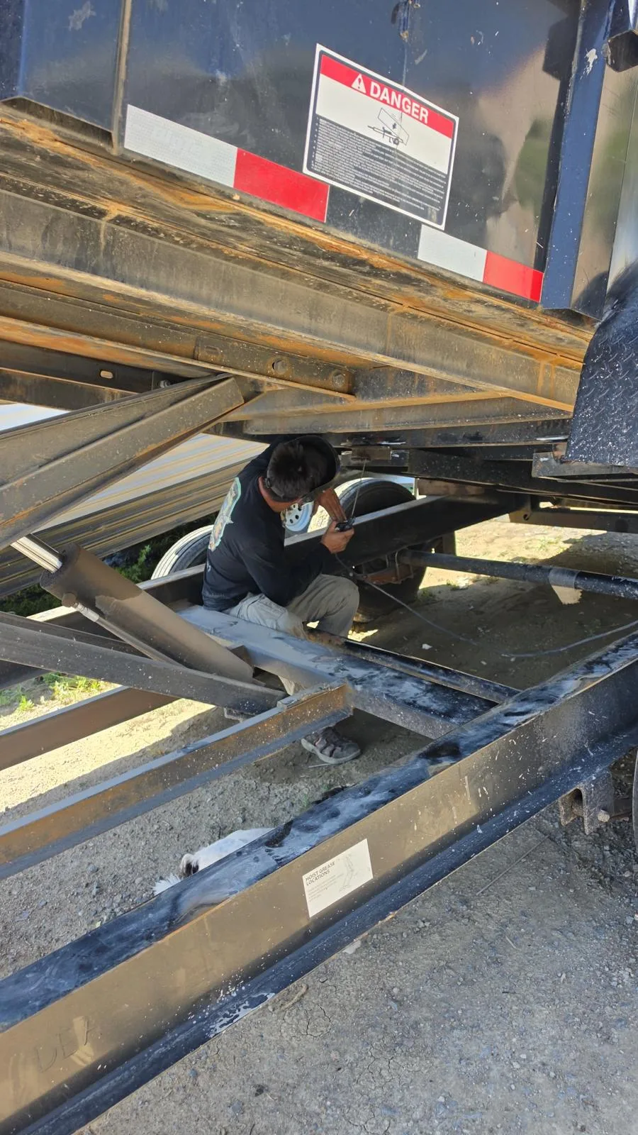 Welder inspecting a gooseneck trailer frame for repair